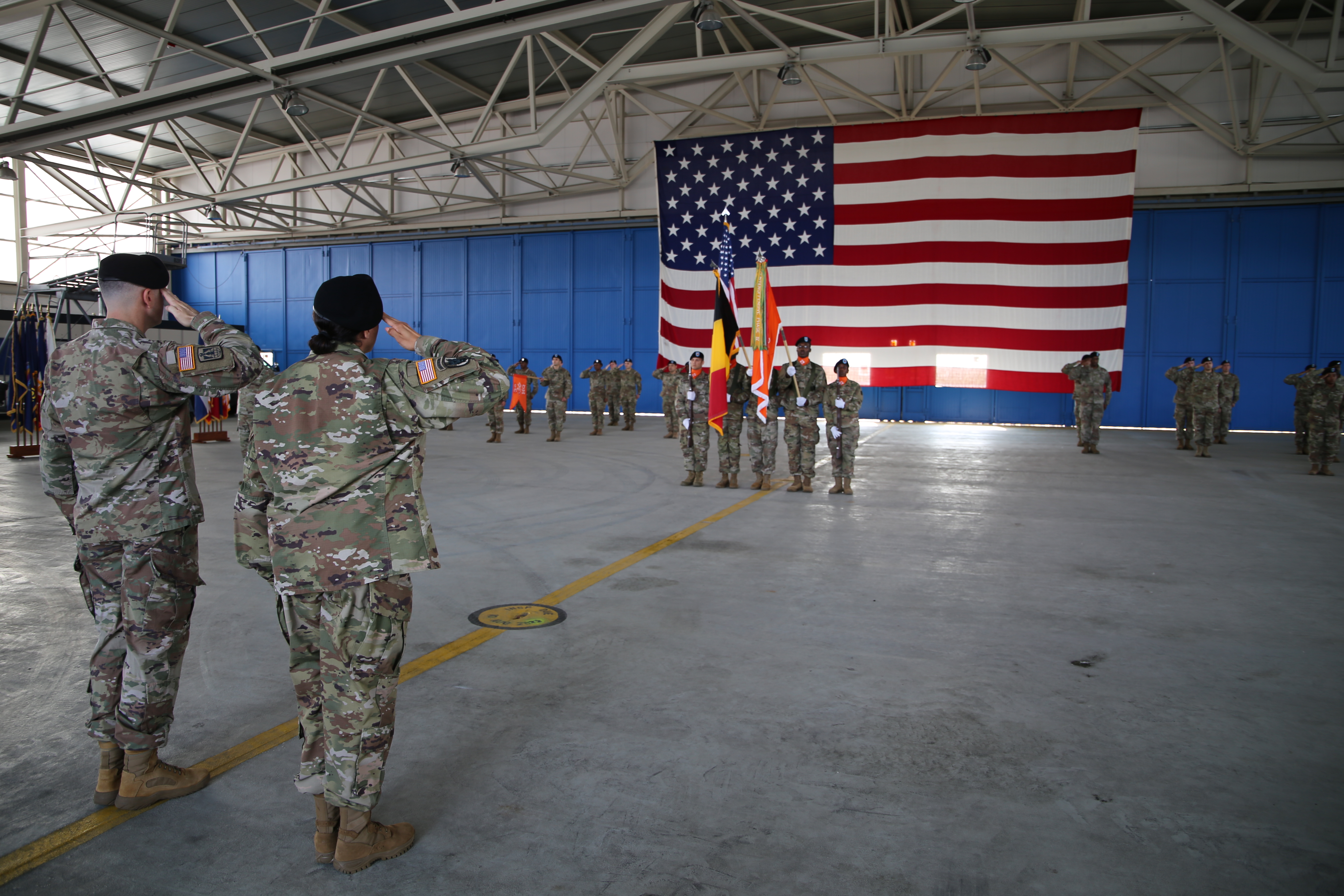 A photograph of two individuals saluting a large American flag at a ceremony