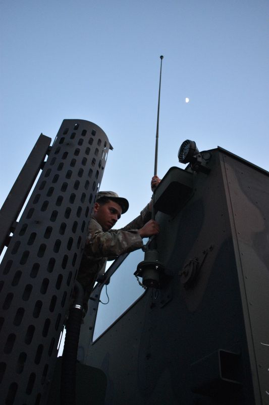 Antenna work Soldier affixes antenna onto back of cab of Bobtail tractor trailer under a clear sky with partial moon