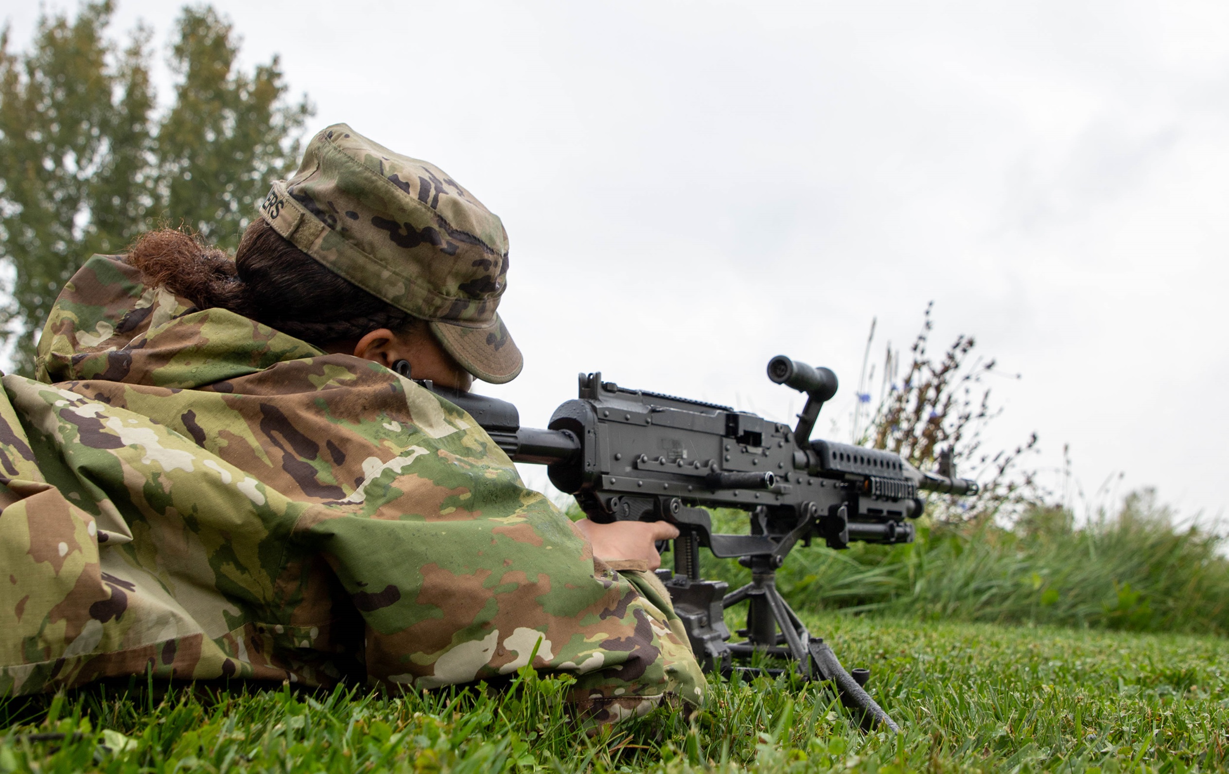 Female Soldier lies on the ground nd aims M240 machine gun during training.