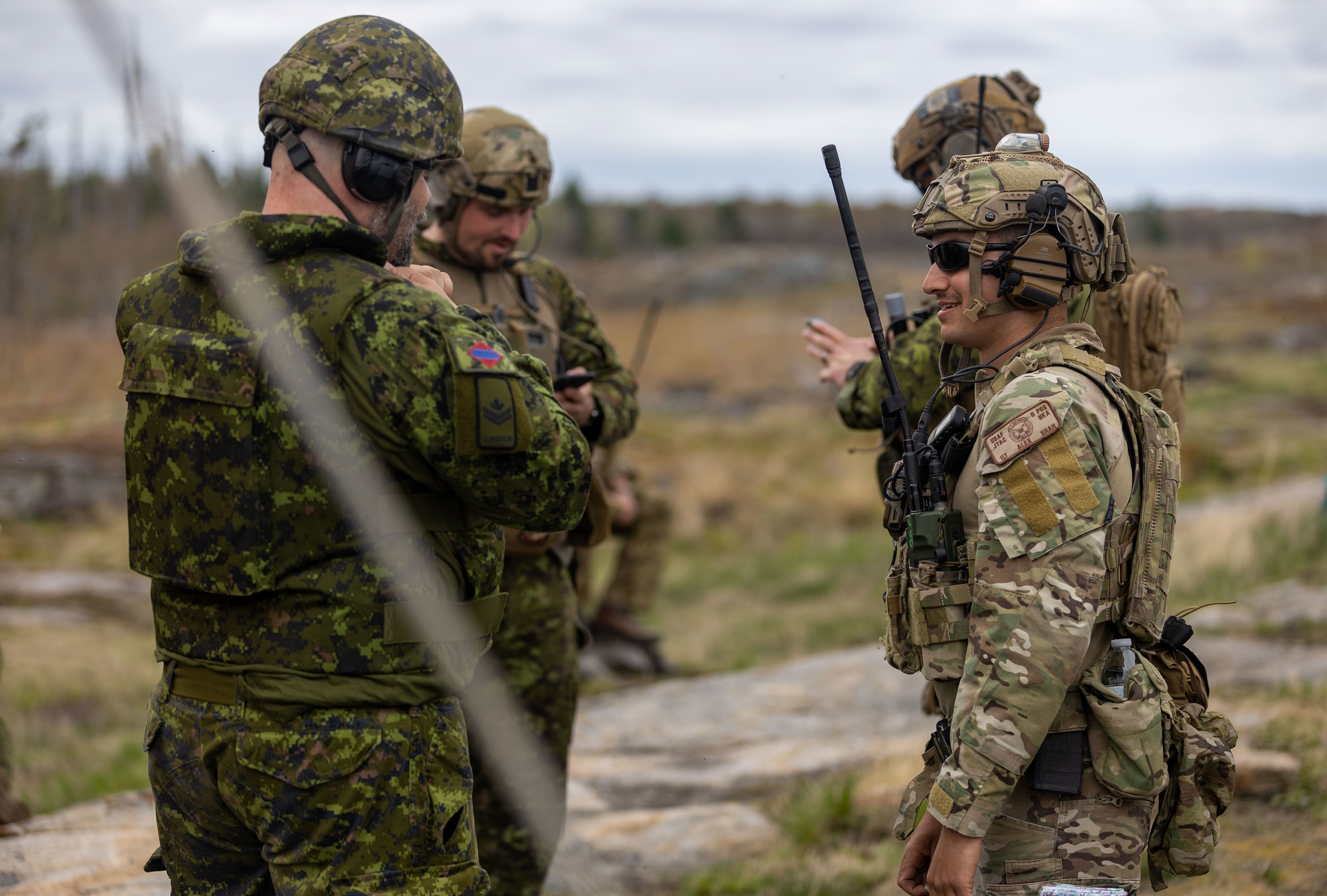U.S. airmen and Canadian soldiers talk while standing together.