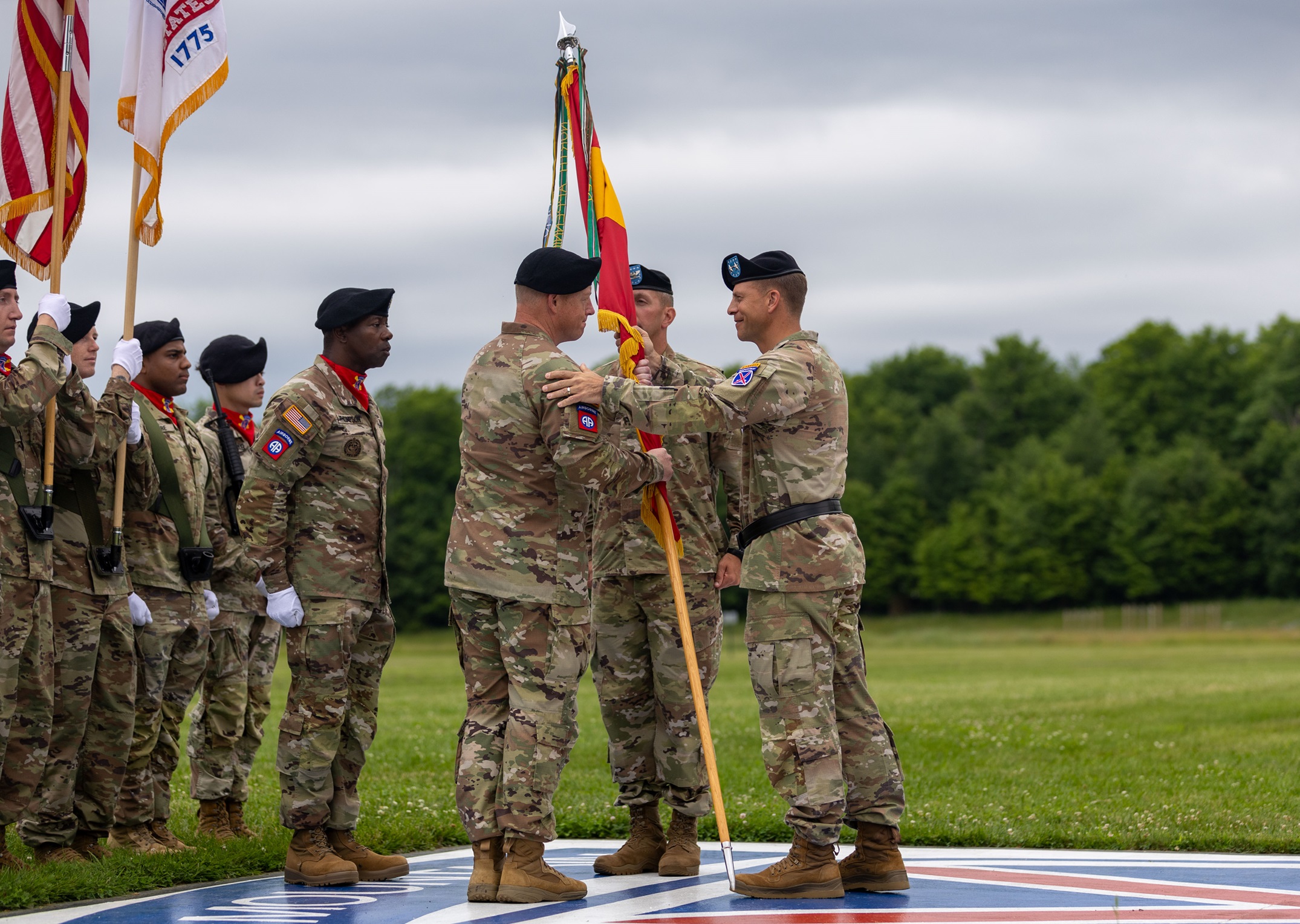 Division commander passes guidon to incoming DIVARTY commander, other Soldiers look on.