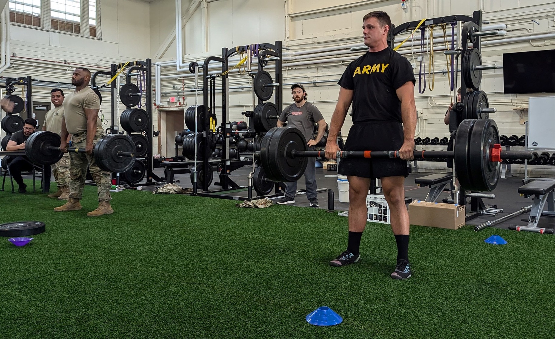 Soldiers deadlift heavy weights inside gym.