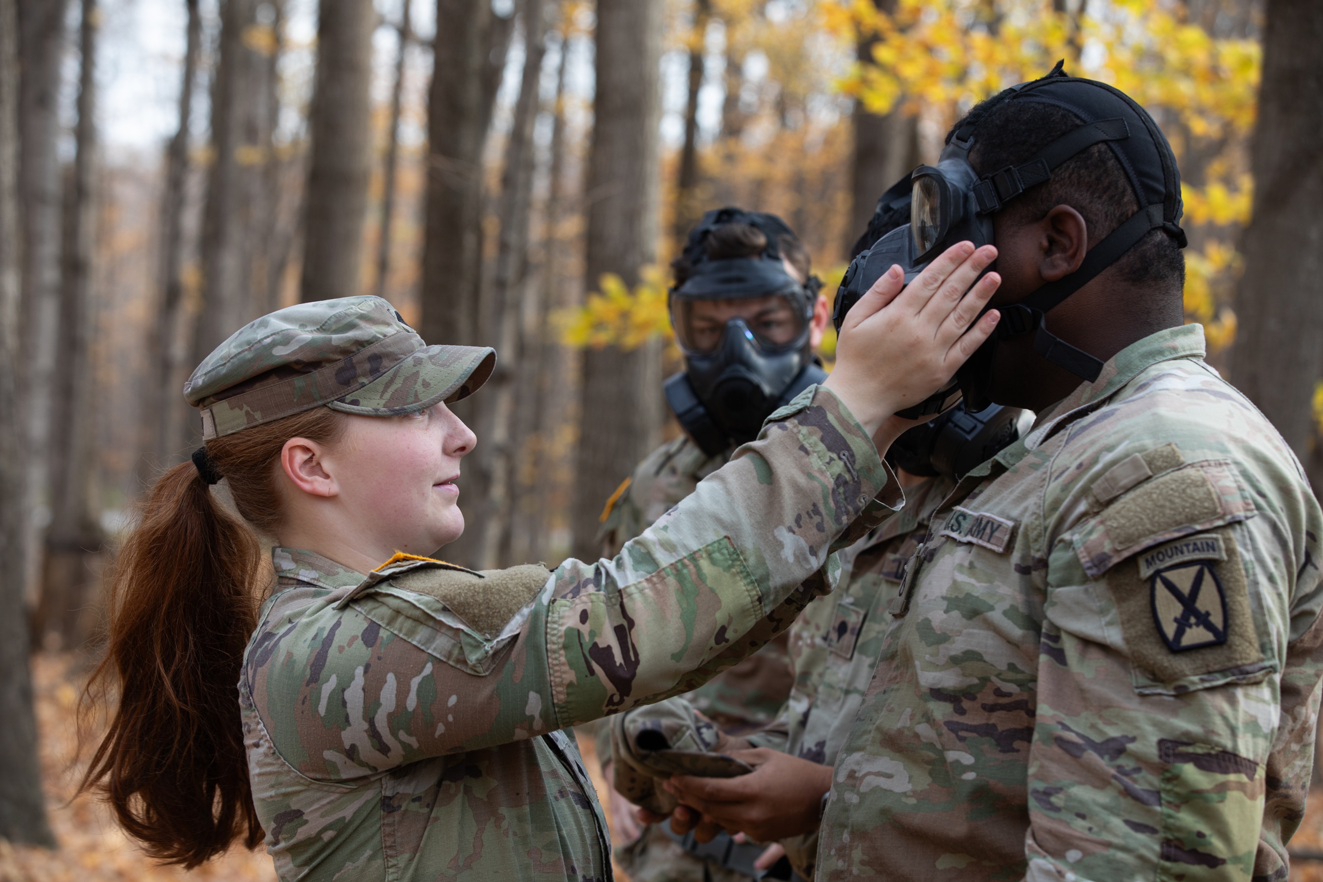 Female Soldier adjusts male soldier's gas mask during training. 
