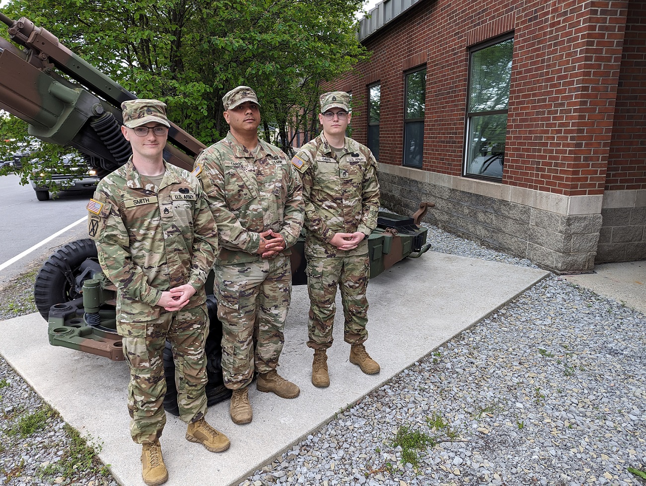 Three Soldiers stand in front of howitzer