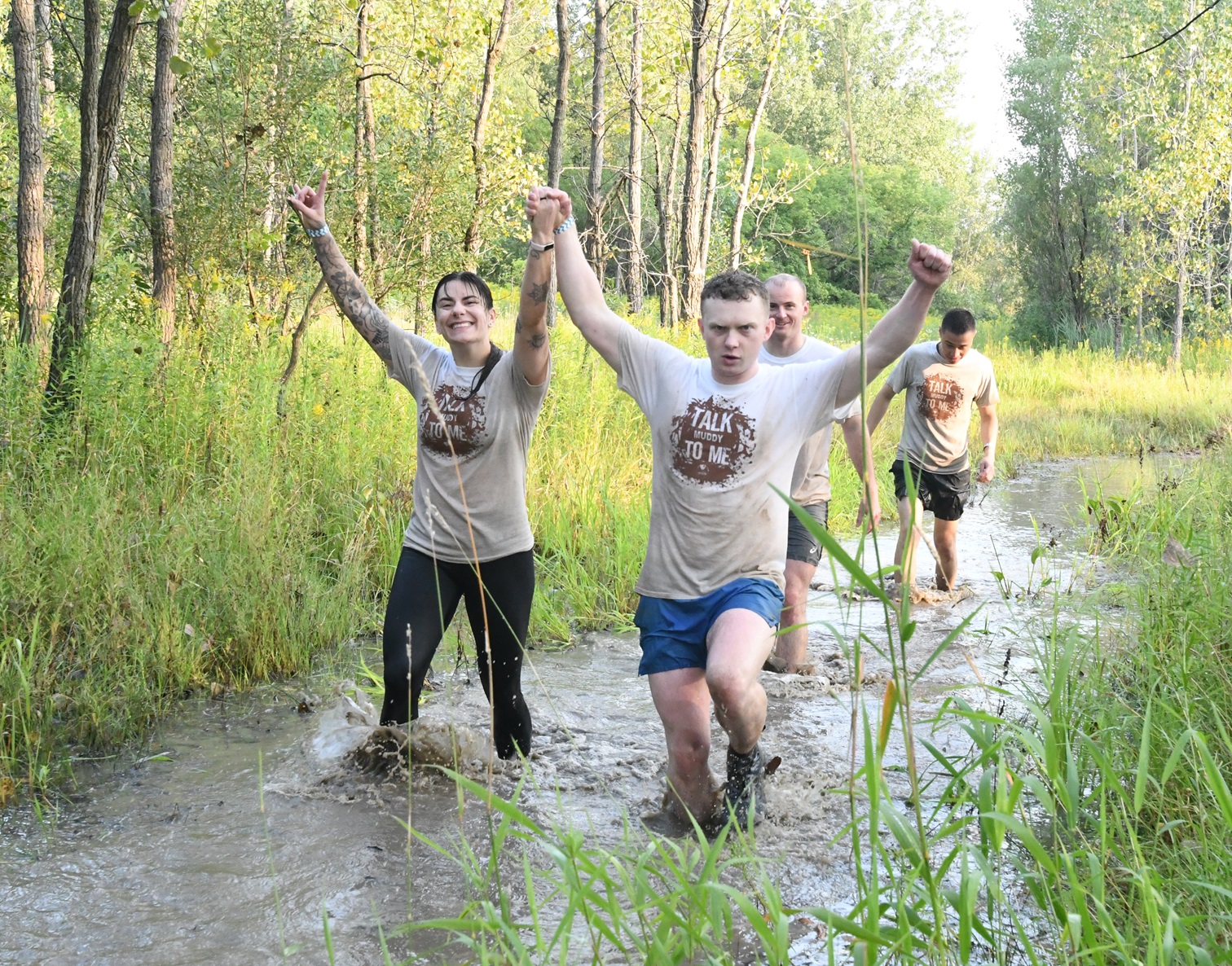 Participants splash through muddy water with arms raised during 2024 Mountain Mudder.