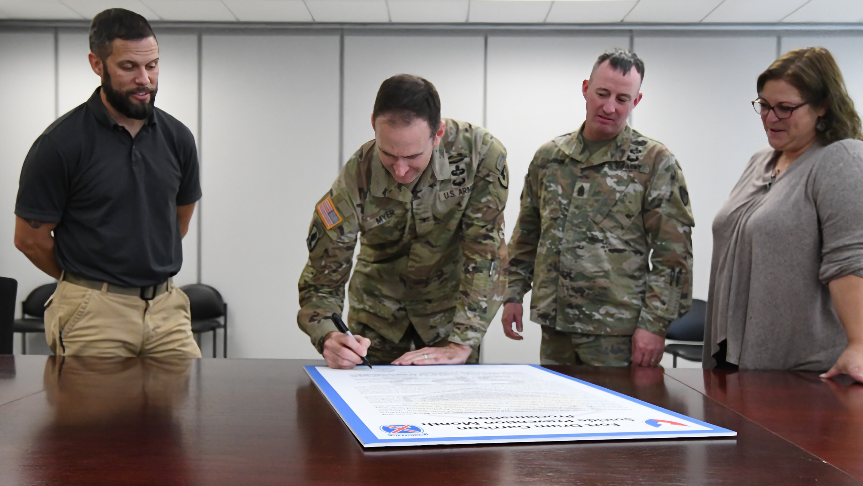 Garrison leaders sign Suicide Prevention Month proclamation while man and woman look on.