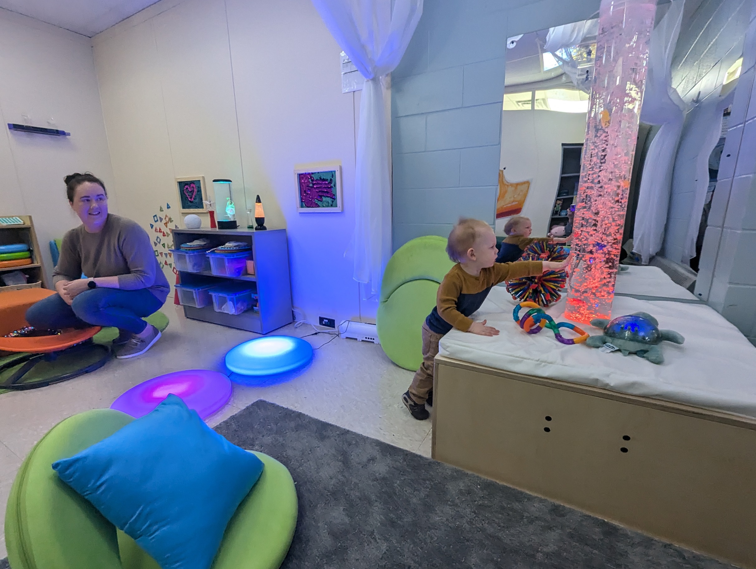 A mom watches as her young son exployes the Fort Drum Sensory Sharing Space filled with soft colors. fabrics.