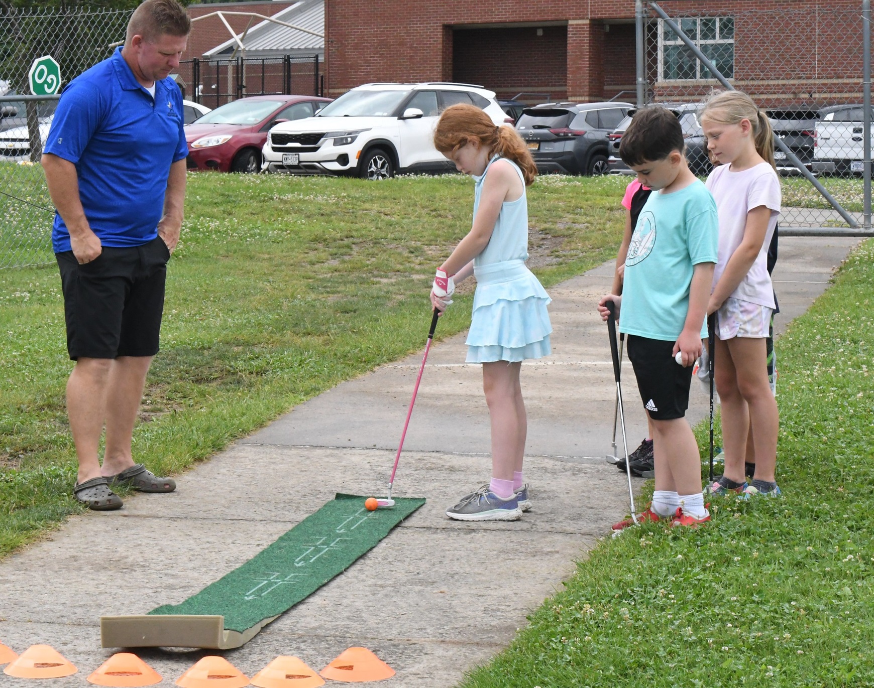 Girl practices putting while instructor and other chidlren look on at CYS Summer Camp.