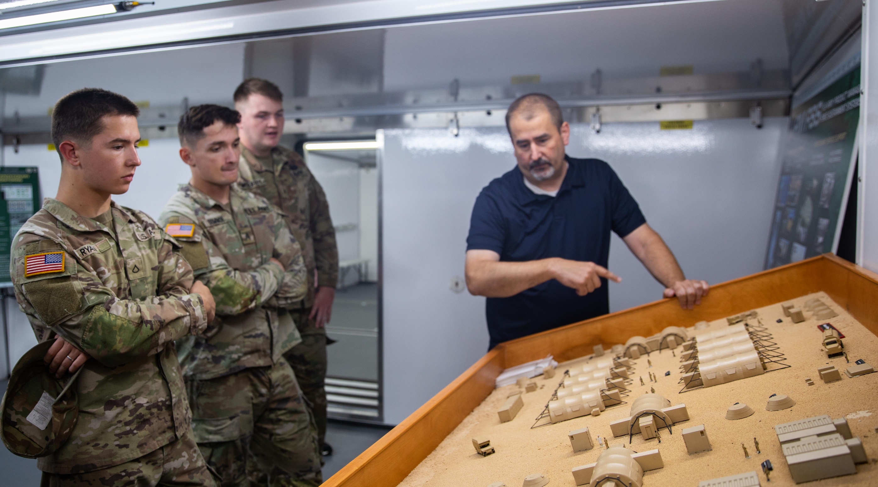 Soldiers examine sand table displaying miniature structures.