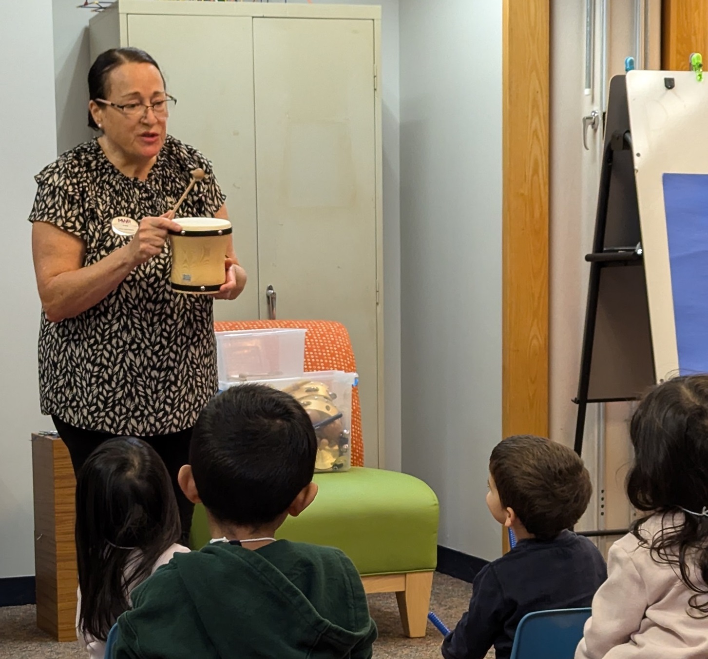 Woman demonstrates for children how to play a musical instrument.