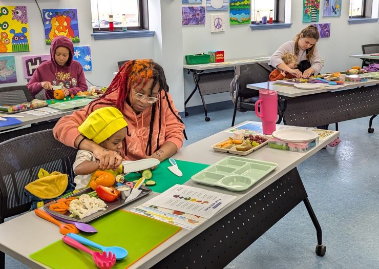 Mothers and kids cut vegetables at tables during Sensory Eating Adventures class.