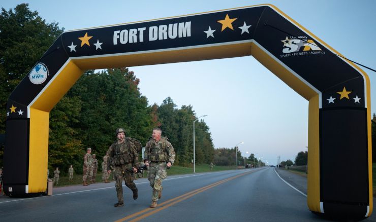 Soldier completes 12-mile ruck march while senior NCO encourages him.