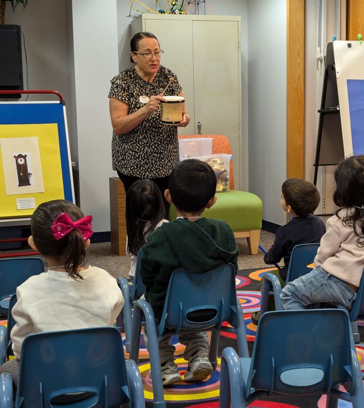 Woman demonstrates how to use a musical instrument for young children in the library.