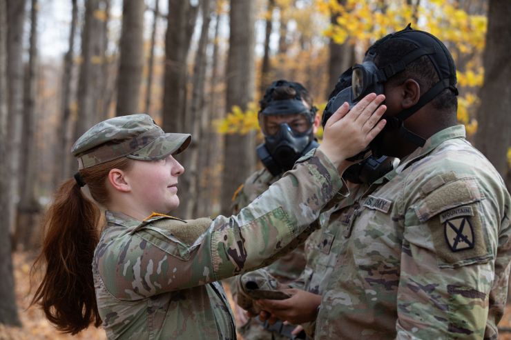 Female Soldier adjusts male soldier's gas mask during training. 