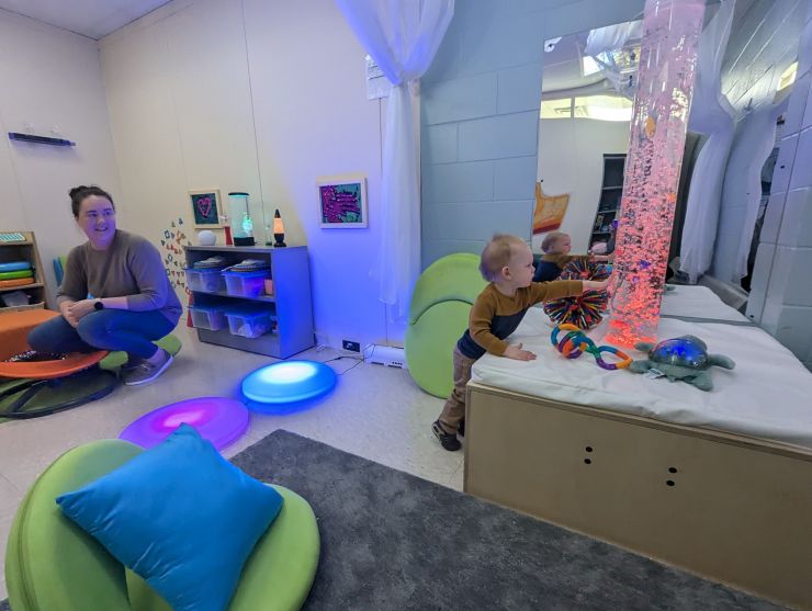 A mom watches as her young son exployes the Fort Drum Sensory Sharing Space filled with soft colors. fabrics.