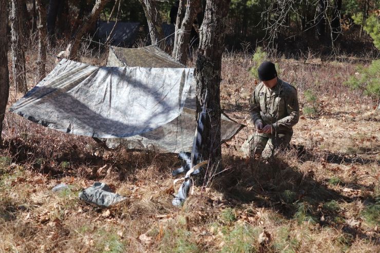 Photo: A Soldier builds a shelter in the woods at Fort McCoy.