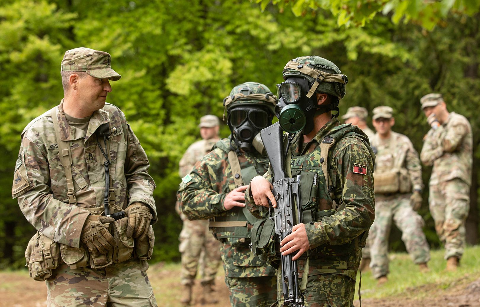 Allied soldiers speak to a U.S. Army observer during a simulated gas attack at a JMRC exercise.